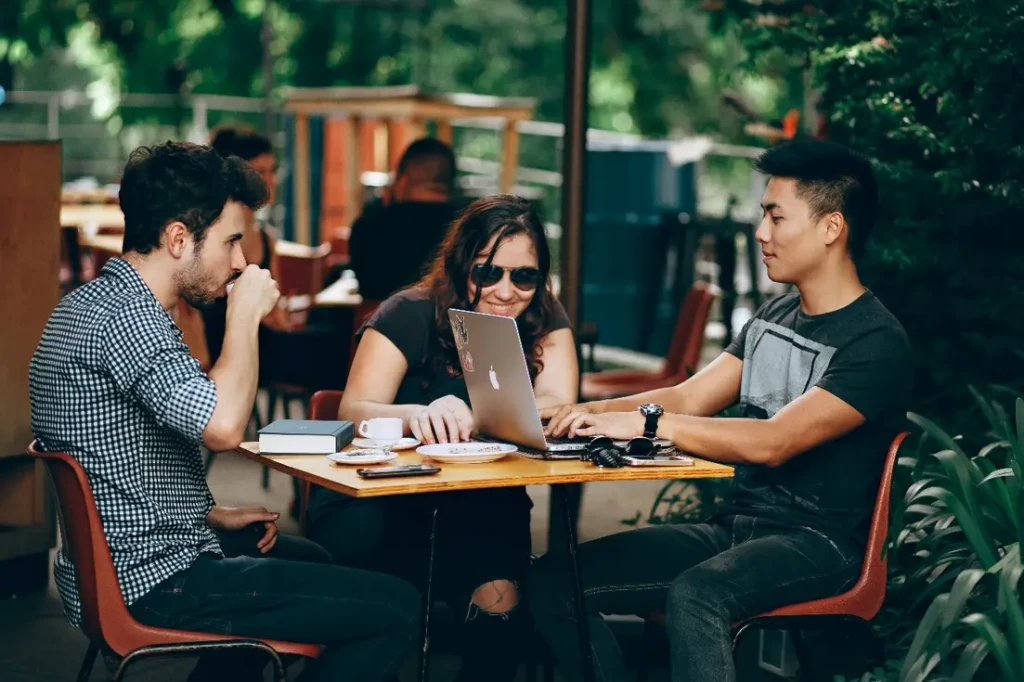 Three people sitting at a table with laptops, having a meeting while enjoying a cup of coffee.