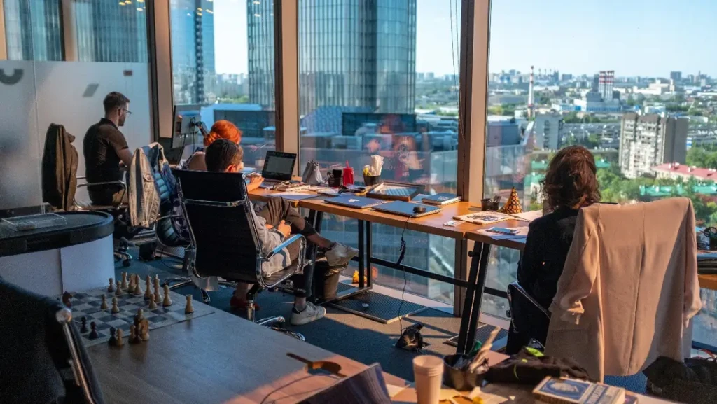 Office workers at desks with a cityscape view in the background.