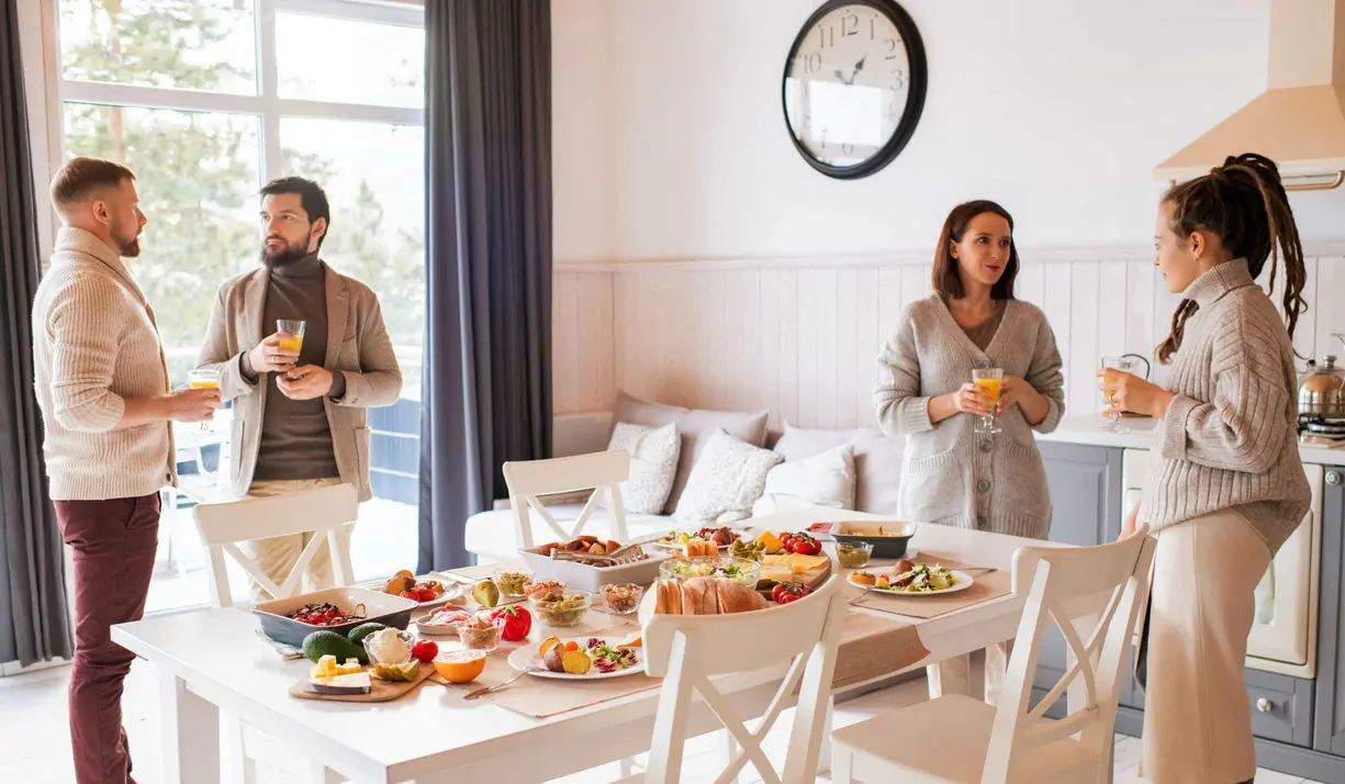 A diverse group of people having a conversation around a table filled with delicious food.