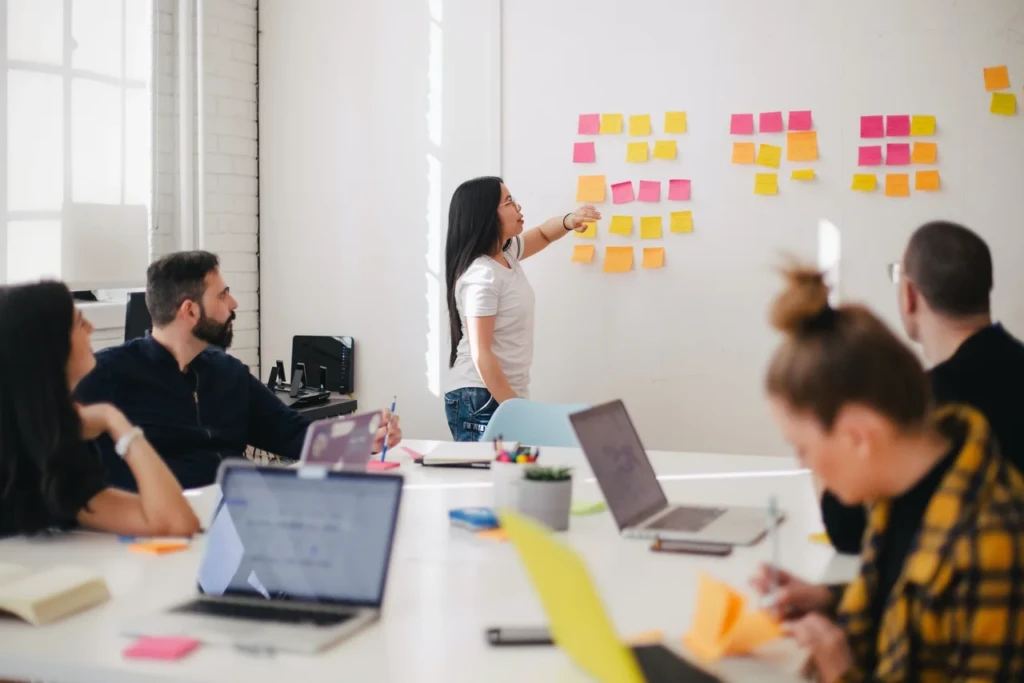 A diverse team collaborating at a table, surrounded by sticky notes on a whiteboard, brainstorming ideas.