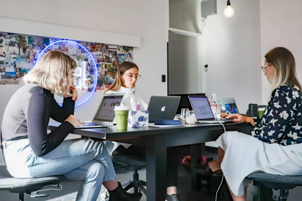  Group of women collaborating at a table, each focused on their laptop screen.